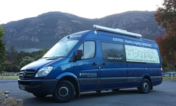 Blue van with ASPREE Healthy Ageing Biobank printed on the side, is parked before high rocky mountains in the background