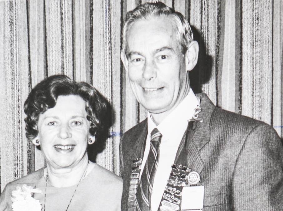 Black and white photo of a man and woman standing together. The man has several badges on his suit jacket. 