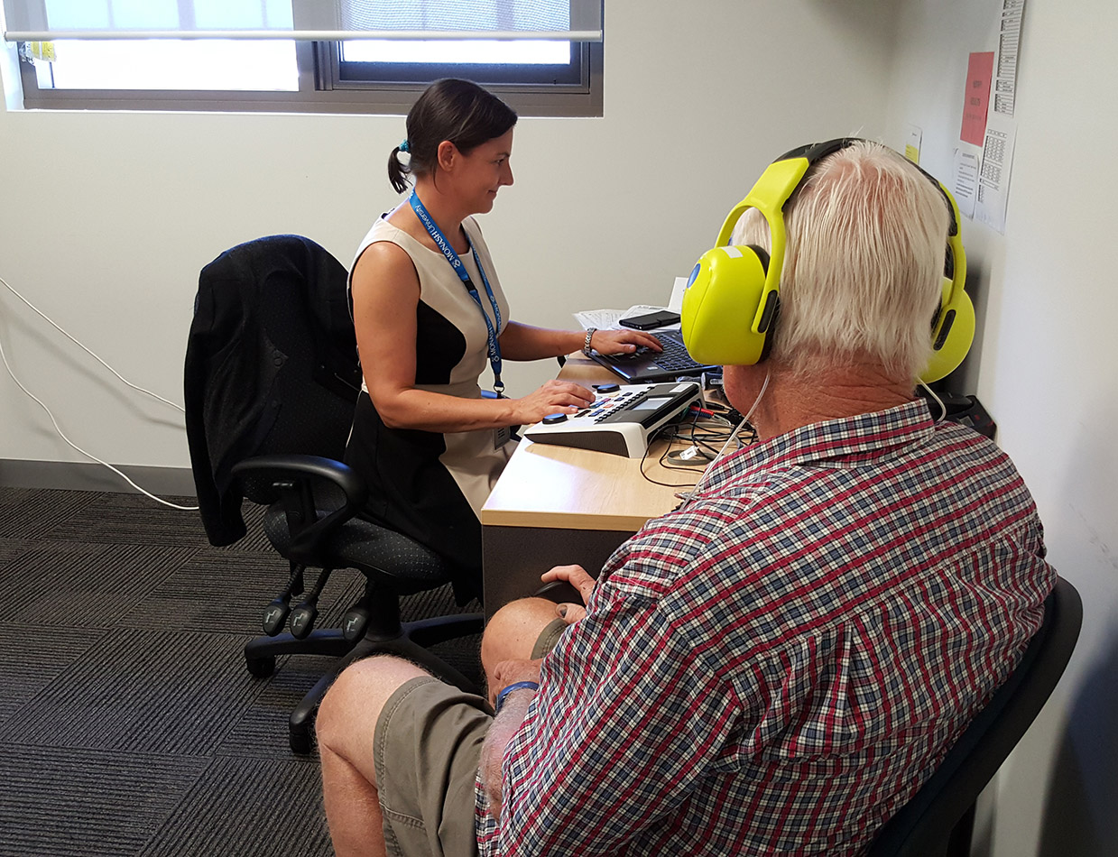 An older male with yellow earphones has a hearing test in an office