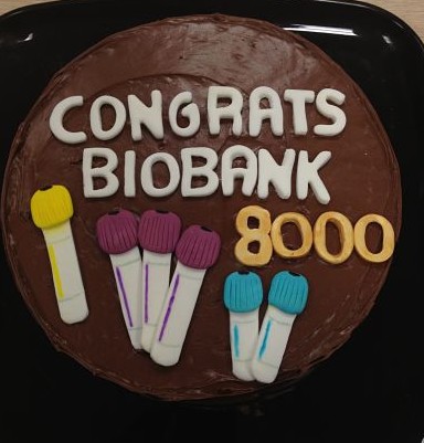 Round chocolate cake with Congrats Biobank 8000 written in white and orange icing.